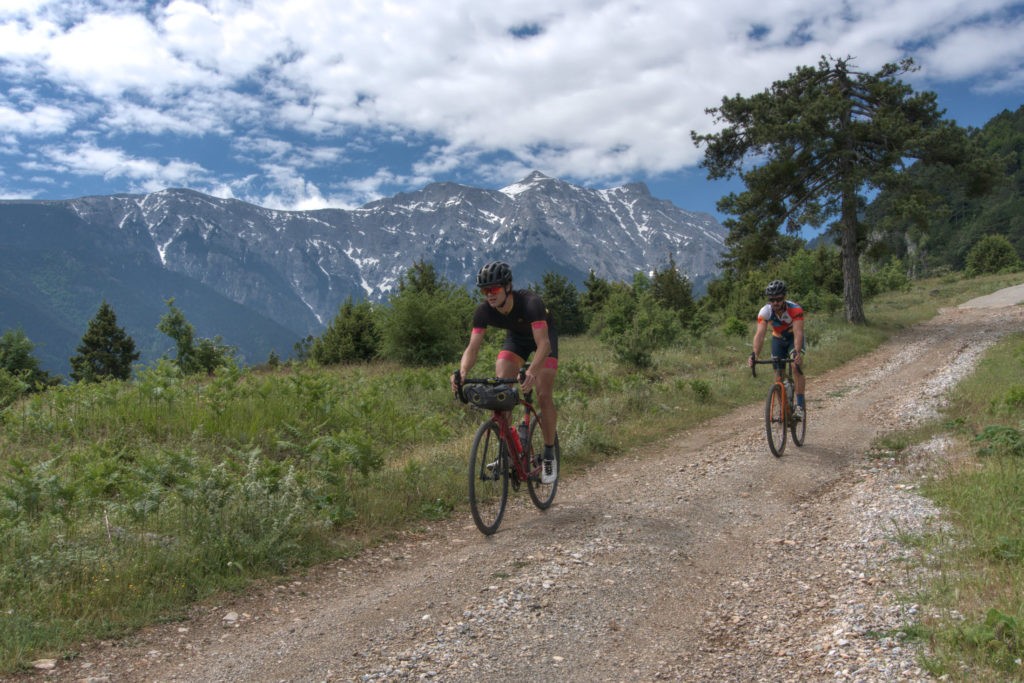 Cyclists cycling on a great gravel roads with view on the Olympus glaciers.