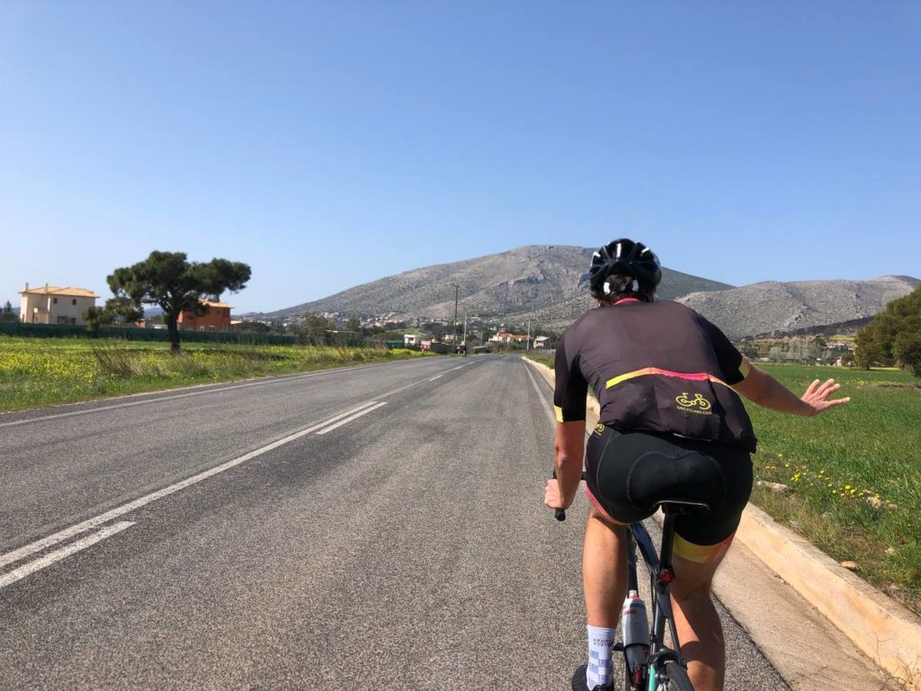 Road cyclist traversing green fields in Athens